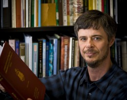Photo of professor Thomas Rooney holding a book in front of a book case.