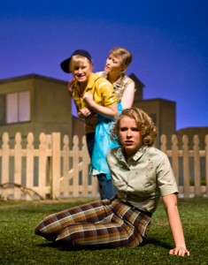Photo of a scene from Picnic featuring a young woman in the foreground with two women fighting behind her.