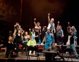 Photo of the cast standing on tables and pumping their fists in the air.