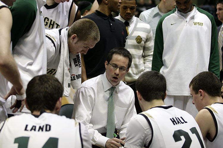 Picture of head basketball coach Billy Donlon instructing his players on the court as they huddle around him.