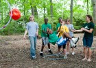 Photo of Wright State students and little sibs hanging from a rope trying to toss a red ball through a hoop during an activity at the Wright State woods.
