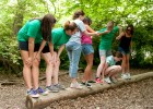 Photo of several little sibs and Wright State students trying to balance on a log.