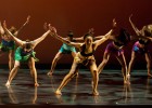 Photo of several dancers bent over with arms raised.