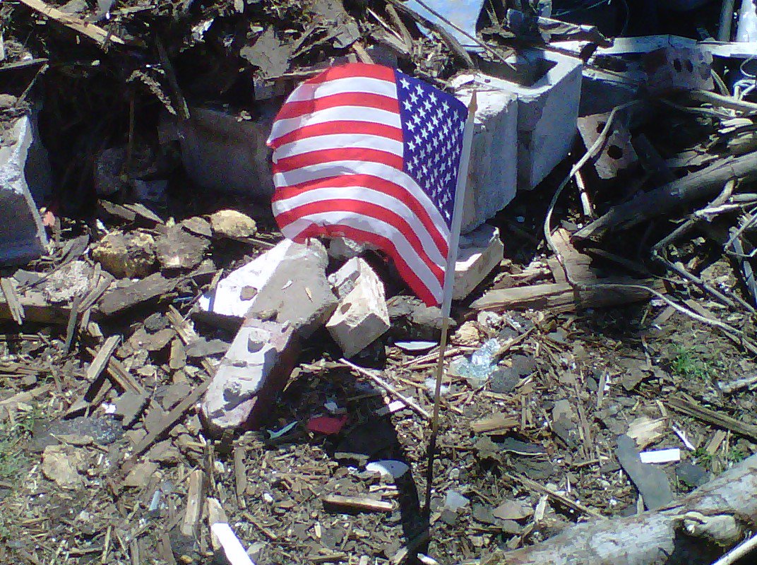 Photo of a small American flag planted in the gound at the site of a destroyed home.