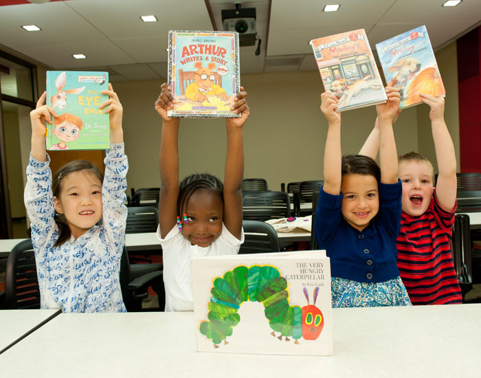 Photo of four kids smiling holding books over ther heads.
