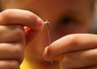 Photo of an extreme close up of a sewing needle being thread by a young girl.