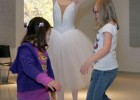 Photo of a student dressed as a ballerina teaching two young girls to dance.
