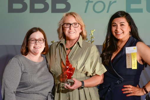 Three people standing together, smiling at the camera. One is holding an award.