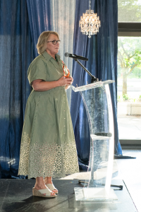 A person in a dress standing at a podium speaking into a microphone while holding an award.