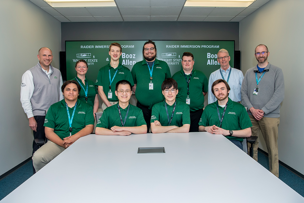 Eleven people stand and sit behind a table, wearing an assortment of polos and and jackets.
