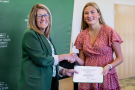Two people are shaking hands, smiling at the camera. One person is holding a certificate.