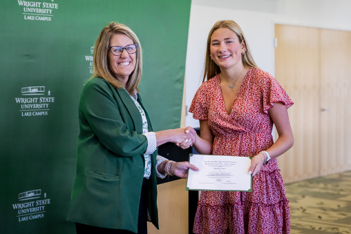 Two people are shaking hands, smiling at the camera. One person is holding a certificate.