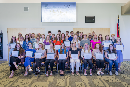 A group of students sit and stand while smiling at the cameras. They are each holding a certificate.