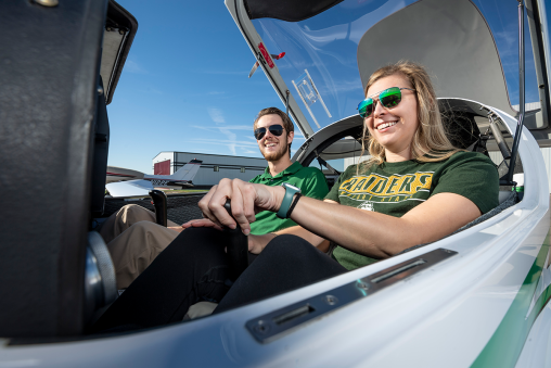 Two students in Wright State apparel sitting in a small plane, smiling at the camera.