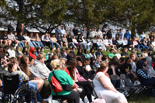 A crowd of people sit in lawn chairs at an outdoor event.