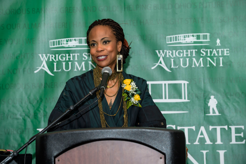 A woman standing at a podium giving a speech. The background behind her reads, "Wright State Alumni."