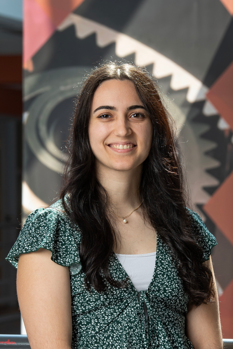 A woman smiles for the camera. Behind her is a banner with a large graphic of an engineering gear on it.
