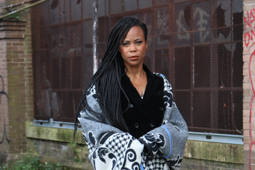 A woman in a cardigan standing in front of an old building with graffiti on some of the walls.
