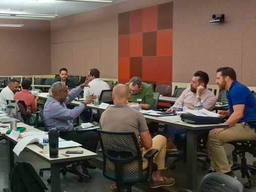 Multiple people sit at classroom tables, working together as a group.