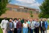 Sixteen people in business attire standing in front of a brick building. The building is labeled "Raj Soin College of Business."