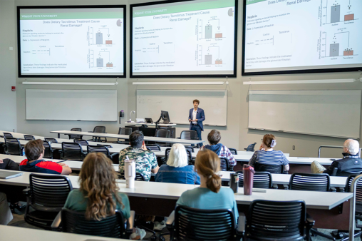 A student stands in front of a classroom, presenting research.