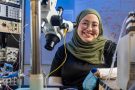 Hana Habib smiling behind the microscope in the Neuro Engineering, Rehabilitation and Degeneration lab.