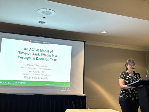 A woman stands at a podium presenting research. The screen behind her reads "An ACT-R Model of Time-on-Task Effects in a Perceptual Decision Task."