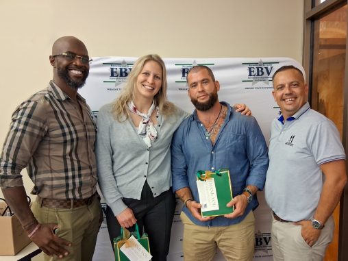 Four individuals stand in front of a backdrop reading "EBV." Two participants are holding gift bags.