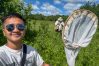 A man stands in a field full of plants, holding up a fly net. A man in the background is examining a finding.