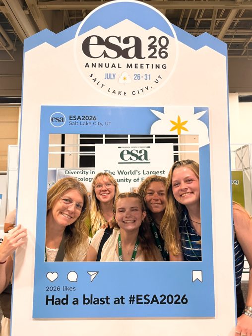 A group of students stand together holding a photoframe that says "ESA 2026 ANNUAL MEETING, SALT LAKE CITY, UT" and "Had a blast at ESA 2026!"