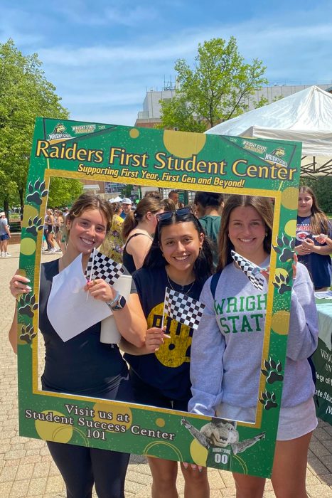 Three students stand inside a large photo frame that reads "RAIDERS FIRST STUDENT CENTER, VISIT US IN STUDENT SUCCESS 101"