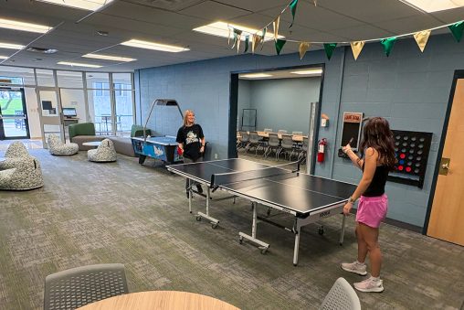 Two students play ping-pong in a recreational room.