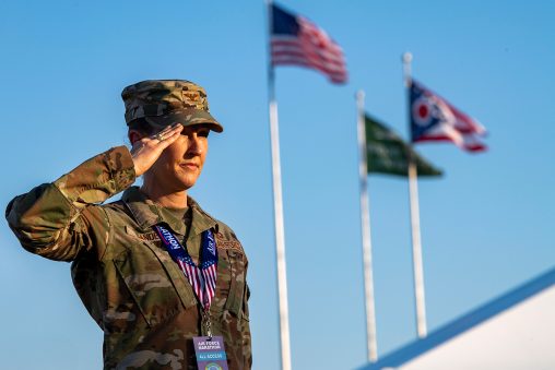 A soldier stands, saluting. An American flag, Wright State University flag, and State of Ohio flag fly behind them.