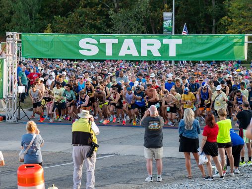 A large amount of runners stand under a "START" banner, preparing to begin a race.