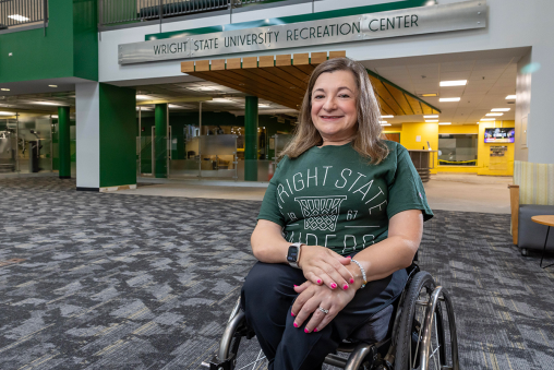 A woman in a wheelchair wearing a Wright State shirt poses outside of the Wright State University Recreation Center.