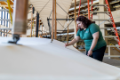 A woman in a Wright State shirt is dusting a life sized model of the Wright Flyer.