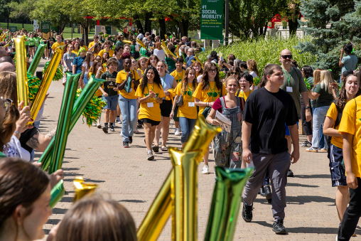 A group of students in Wright State t-shirts walk down a sidewalk, being cheered on by staff and faculty members.