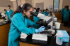 A woman in a lab coat looks into a microscope in a lab.