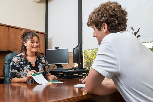 A career consultant sits behind a desk, enthusiastically showing a student a flyer.
