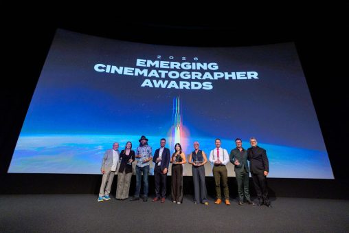 Nine individuals stand on stage holding awards. The screen behind them reads "Emerging Cinematographer Awards."