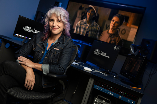 A woman sits in an editing room in front of a computer screen reading "Wright State University Motion Pictures." A tv screen behind her depicts two women.